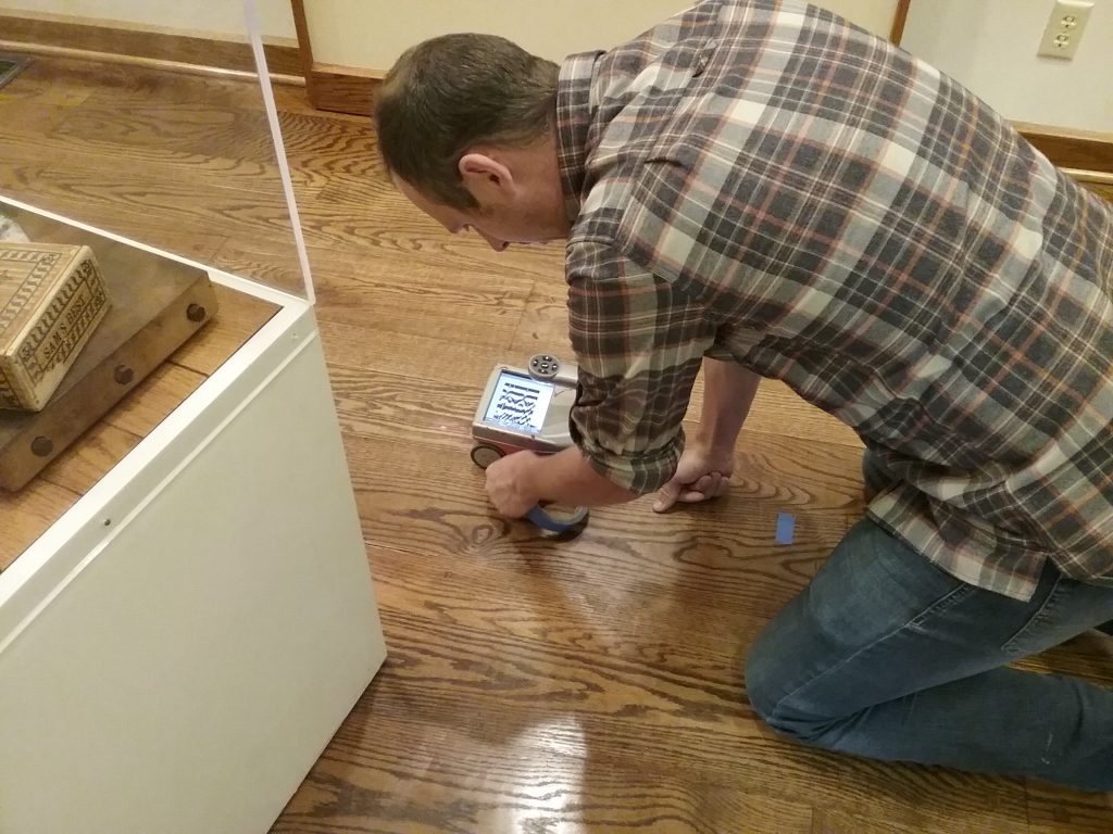 Brandon Mikelson from American Engineering Testing, Inc. using ground penetrating radar to find sleepers under the floor in the Z.N. Barnes Room at The Charles A. Weyerhaeuser Memorial Museum, July 26, 2019. He is marking the sleepers with blue tape as he finds them.