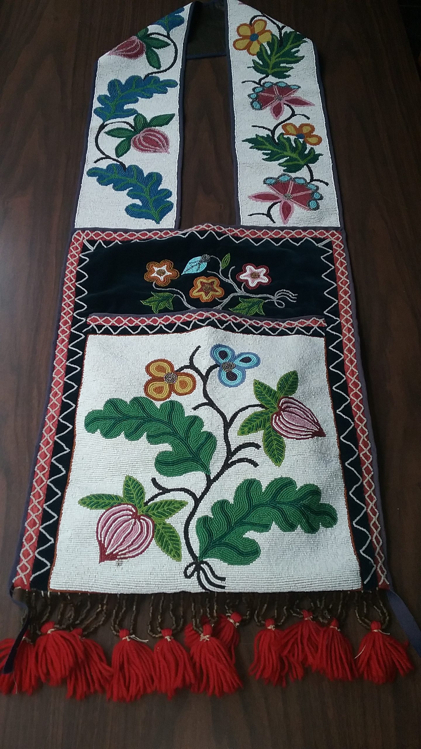 Ojibwe Gashkibidaagan Owned by Ethel Gourd Hall: This Ojibwe gashkibidaagan (bandolier bag) was purchased by Ethel (Gourd) Hall in 1910 at Walker, Minnesota, on Leech Lake. Ethel and her husband Ralph lived at Round Lake in the Randall area of Morrison County. Ethel’s father was Benjamin Franklin Rattling Gourd of the Cherokee Nation. He purchased land in Morrison County in 1909 and brought his family from Oklahoma in 1909/1910. The beading on this bag is spot-stitch applique. Note the floral motif, which includes gear flowers above the pocket and flower buds on the pocket and strap. The strap features an asymmetrical design. MCHS collections, #1954.8.1.