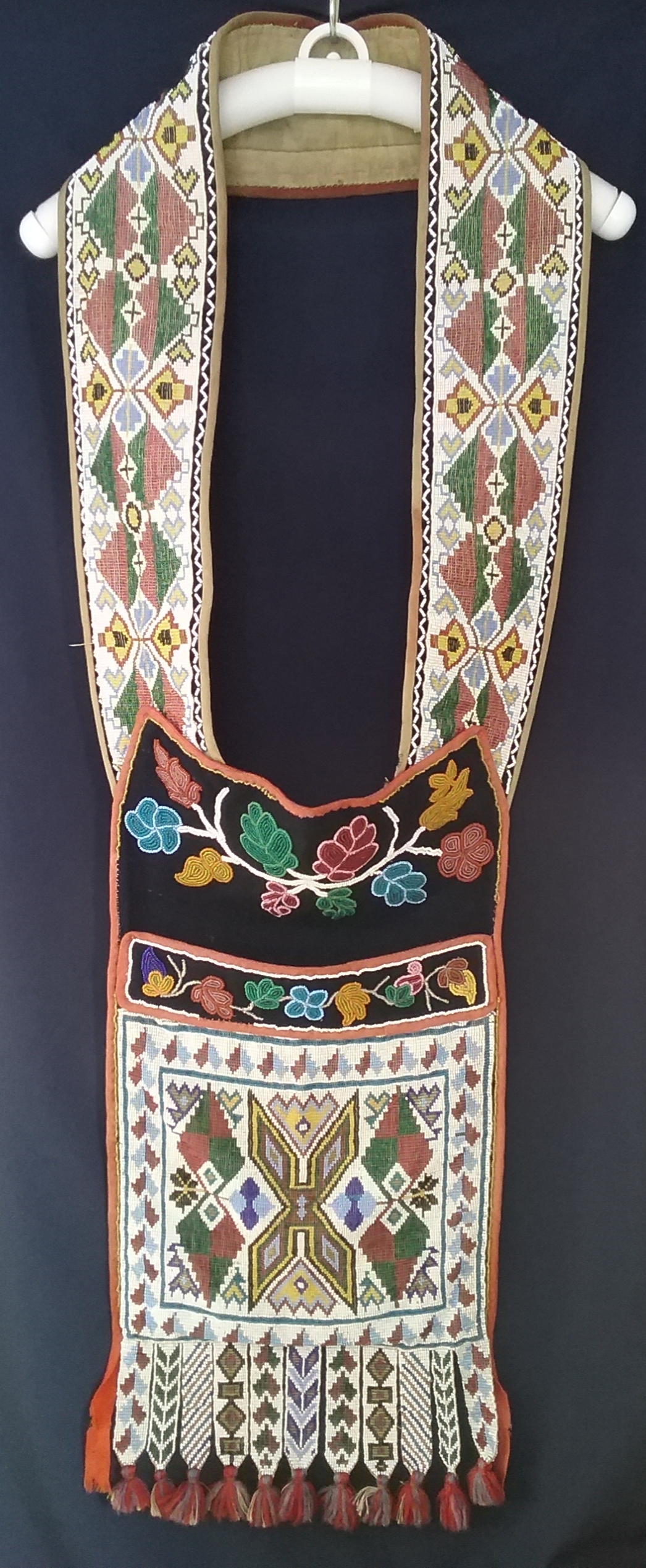 Ojibwe Gashkibidaagan Owned by Nathan Richardson: This Ojibwe gashkibidaagan (bandolier bag) was presented by Mille Lacs Band Chief She-bosh-king to Nathan Richardson (called the Father of Morrison County) in 1884 for his work in assisting the Band with legal matters. The front panel, strap, and fringe feature loom-woven beading, while the sections at the top of the pocket and above the pocket are done in spot-stitch applique. Note the symmetry within the beadwork on the strap and the large X in the center of the pocket. The X was a common motif for Ojibwe loom-woven gashkibidaaganag. MCHS collections, #1940.42.1.