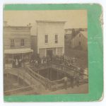 Photo of the Little Falls Ravine at the corner of Broadway and Second Street Northeast, Little Falls, MN. The white building is O. L. Clyde's store. Photo by Neal & Simmons, c. 1883-1885, from the Morrison County Historical Society's collection.