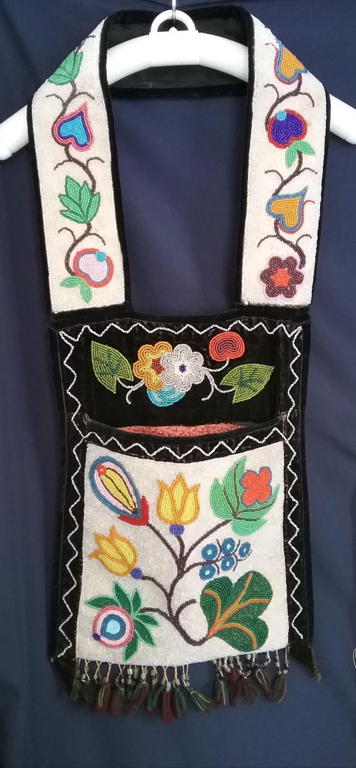 Small Ojibwe Gashkibidaagan: This Ojibwe gashkibidaagan (bandolier bag) was purchased by Upsala resident Jean ­Martinson at a garage sale in Mispah, ­Minnesota. She paid a quarter for it. The bag was originally taken as payment for a grocery store bill in the Turtle Mountains of North Dakota. Jean owned the bag for 20 years before ­donating it to the museum in 1996. The beadwork is spot-stitch applique. Note the floral motif and that the pattern from one side of the strap to the other is not identical. Based on the design, this bag was likely ­produced by someone in the White Earth Band. MCHS collections, #1996.36.3.