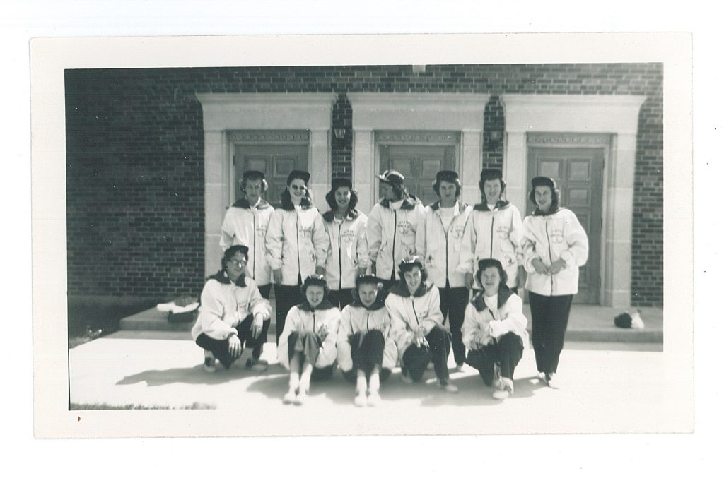 Ski Patrol, Winter Wonderland, Little Falls, MN, 1950. MCHS collections #1992.40.4. - Twelve women dressed in matching winter outfits, white coats with black front zippers and collars and black pants.