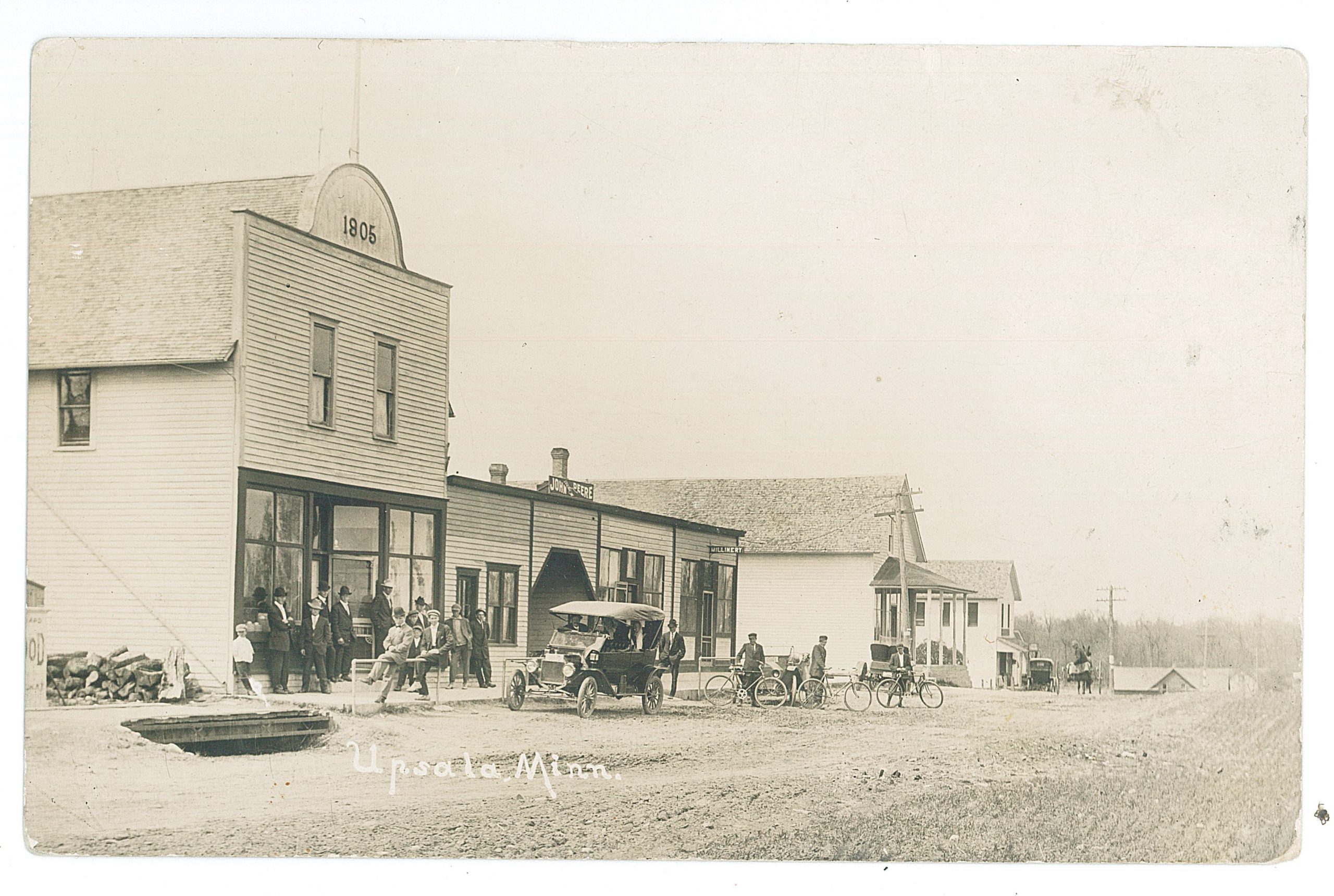 Photo postcard of Main Street in Upsala, Minnesota, c. 1910. Handwritten on the back several businesses are identified, a building built by Upsala Hall Construction Association in 1905 that was purchased by J.S. Borgstrom in 1909, Alfred Pehrson’s groceries, Swedback’s General Store, and a blacksmith shop that burned down later. Donated to MCHS collections by Bill Morgan.