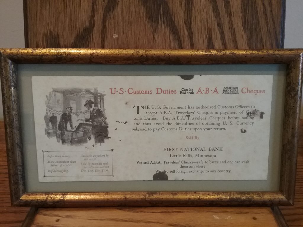 Framed document advertising that First National Bank of Little Falls sold "A.B.A. Travelers' Checks," undated, donated by U.S. Bank.