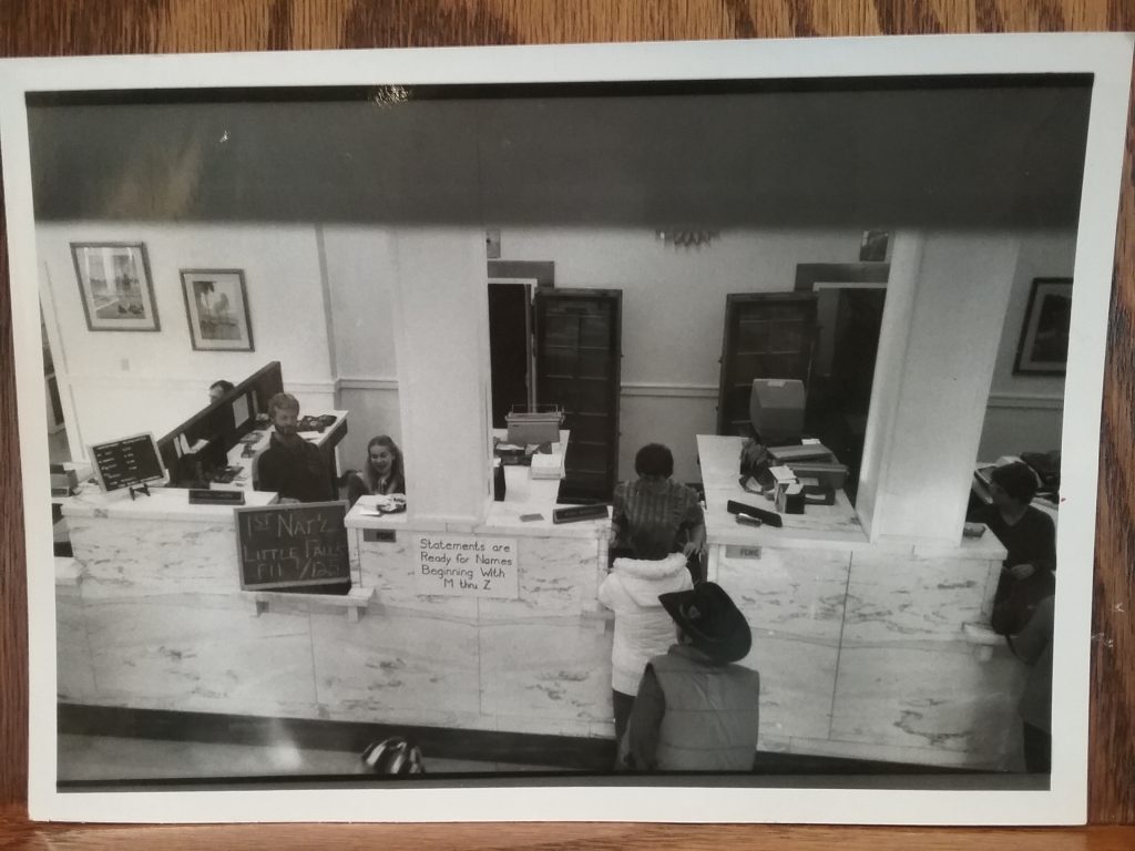 Photo of marble counters with tellers and customers at First National Bank, Little Falls, MN, c. 1980s, donated by U.S. Bank.